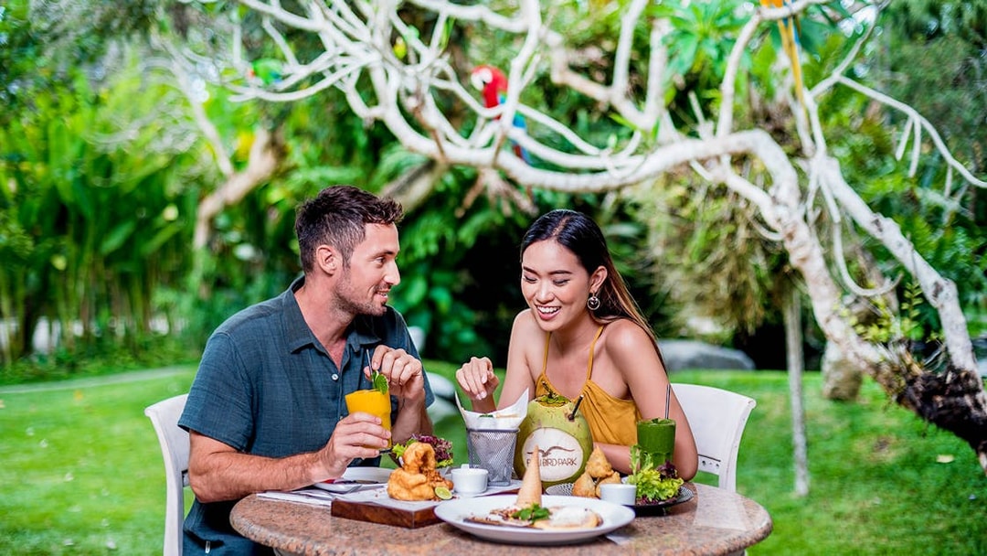 Couple dining outdoors at Bali Bird Park with tropical drinks and food.