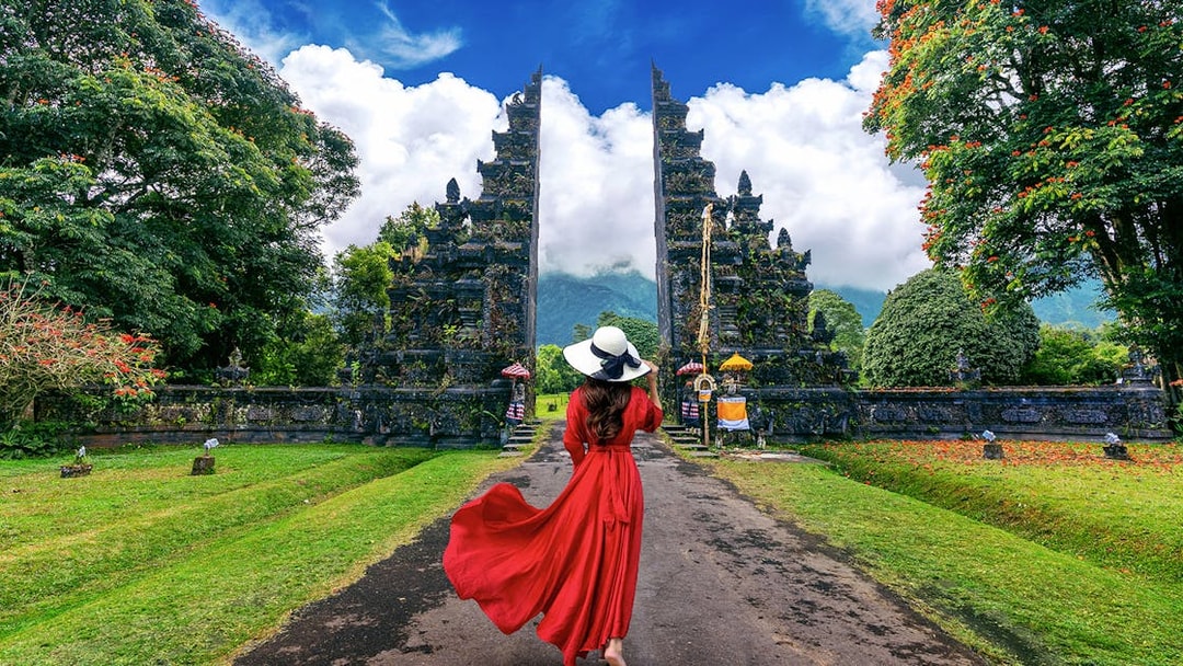 Woman in red dress walking towards Handara Gate in Bali, surrounded by lush greenery.