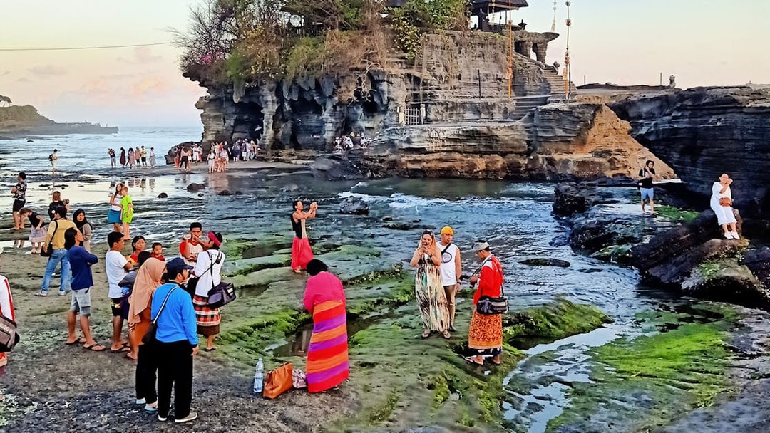 Visitors exploring Tanah Lot temple and rocky shoreline during Bali Private Bedugul, Tanah Lot Sunset Tour.