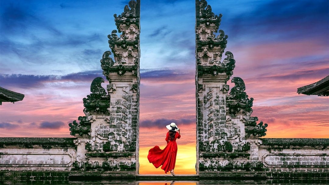 Woman in red dress at Bali's Lempuyang Temple gates during sunrise.