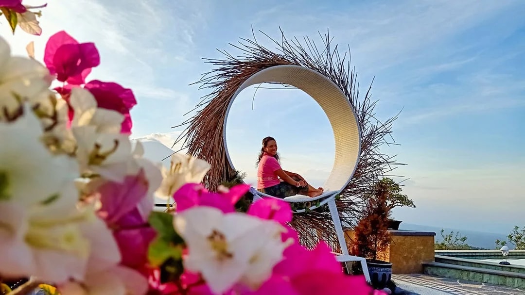 Person sitting in a circular swing with flowers in foreground during Bali sunrise tour.