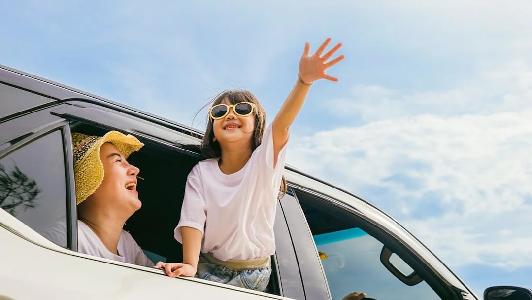 Family enjoying private car transfer with child leaning out window.