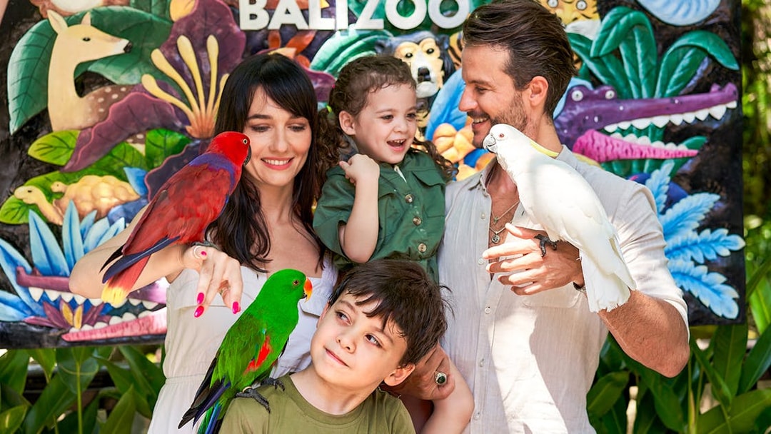 Family enjoying colorful parrots at Bali Zoo entrance.