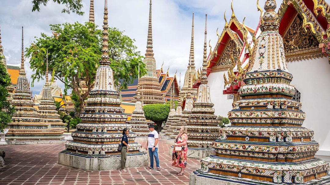 Wat Pho stupas in Bangkok with tourists exploring the temple grounds.