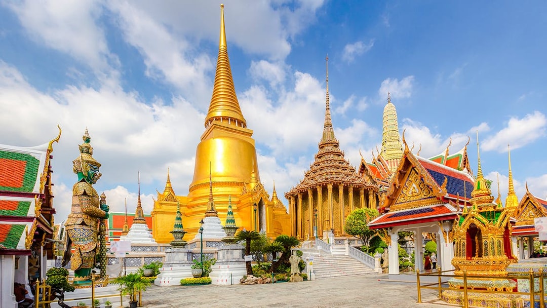 Wat Phra Kaew temple complex with golden stupa and guardian statue, Grand Palace, Bangkok.