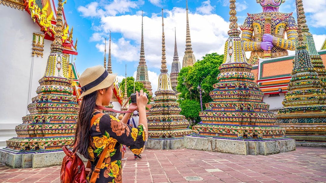 Woman photographing ornate stupas at Wat Pho, Bangkok.