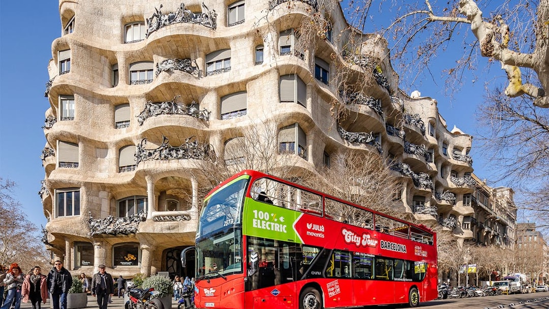 Barcelona hop-on hop-off bus in front of Casa Milà, a Gaudí architectural landmark.