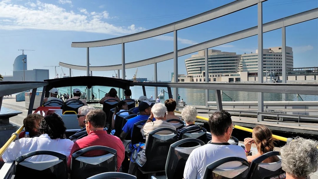 Passengers on Barcelona City Hop On Hop Off Tour bus near waterfront.