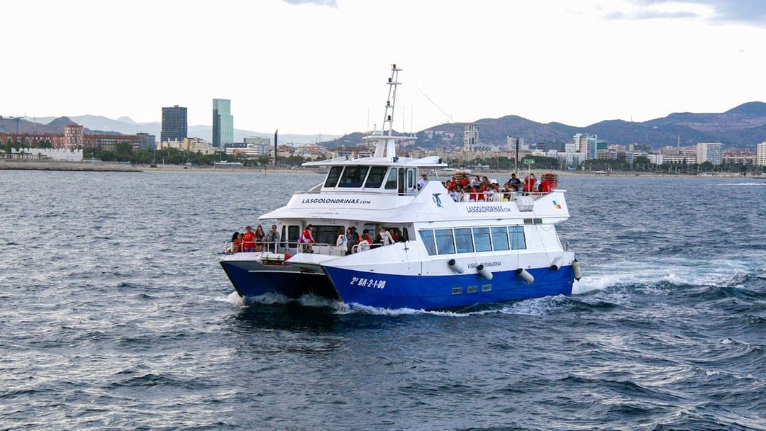 Las Golondrinas boat with tourists cruising near Barcelona coastline.