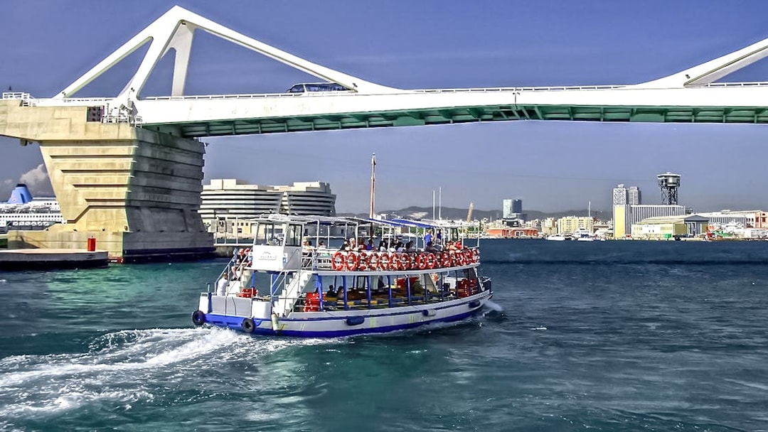 Las Golondrinas boat passing under a bridge in Barcelona harbor.