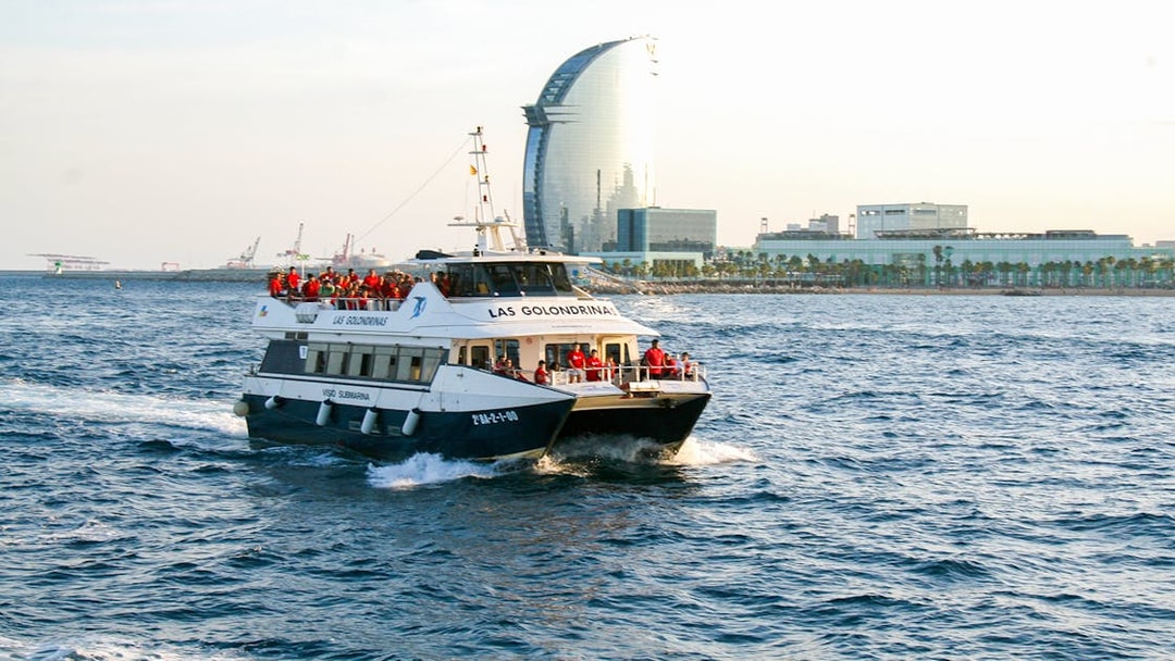 Las Golondrinas boat cruising near Barcelona waterfront with city skyline in background.