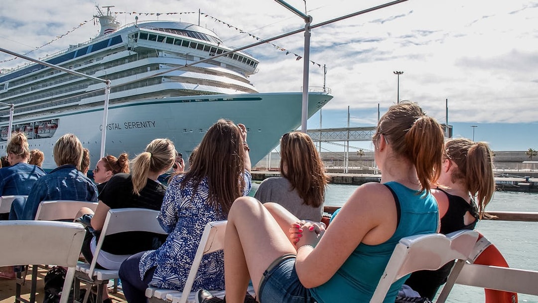 Tourists aboard Las Golondrinas viewing a large cruise ship in the harbor.