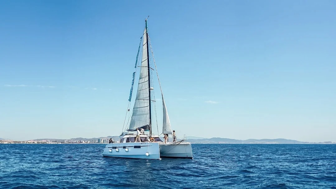 Eco-catamaran sailing near Barcelona coastline.