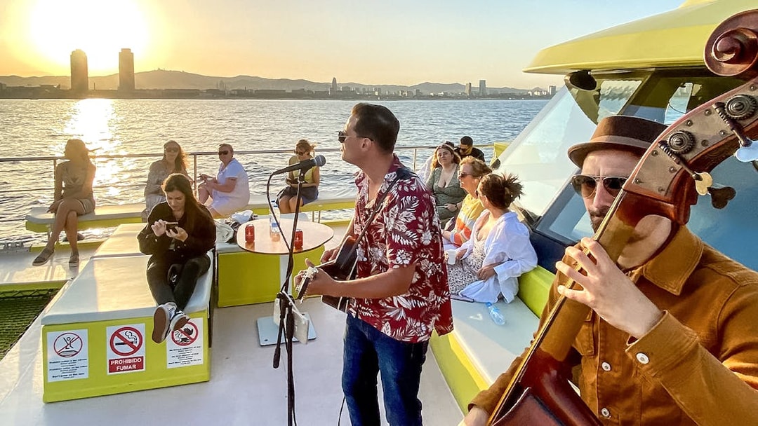 Tourists enjoying live music on a catamaran cruise at sunset in Barcelona.