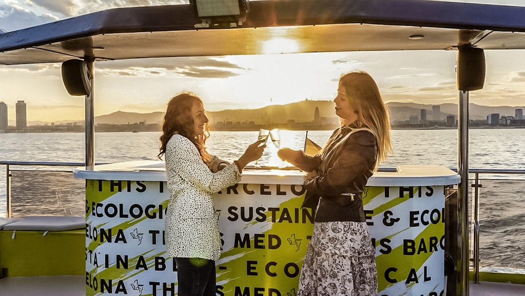 Two people enjoying drinks on a catamaran cruise in Barcelona at sunset.