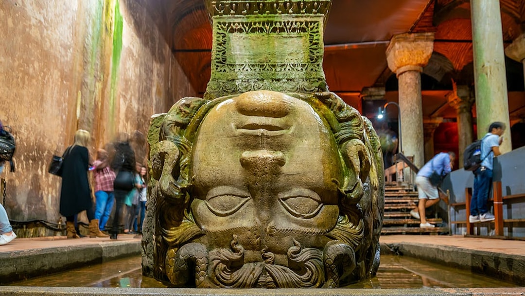Upside down Medusa head at Basilica Cistern, Istanbul, with visitors nearby.