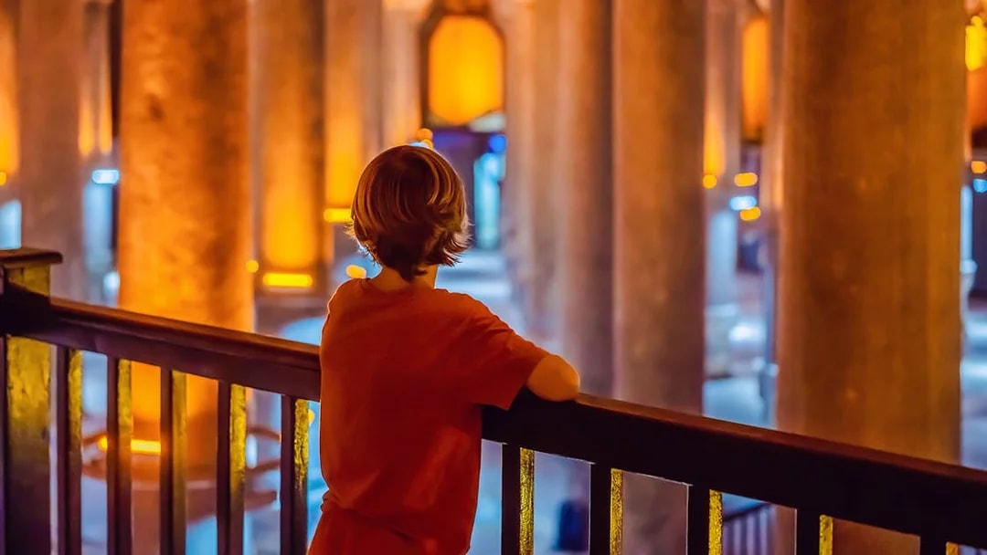 Boy observing illuminated columns in Istanbul's Basilica Cistern.