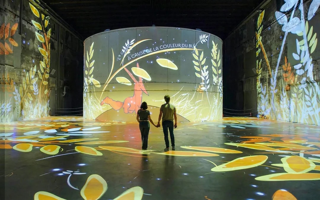 Couple exploring The Little Prince exhibit at Bassins des Lumières, Bordeaux.