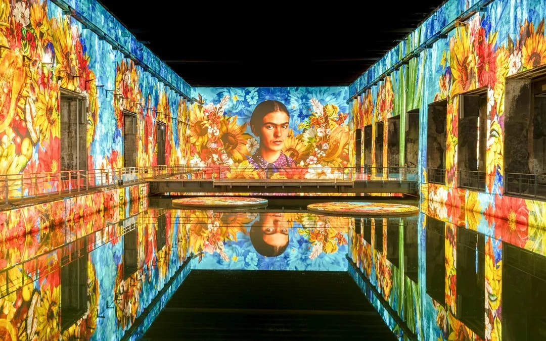 Frida Kahlo artwork projected at Bassins Des Lumieres exhibition, vibrant floral display.