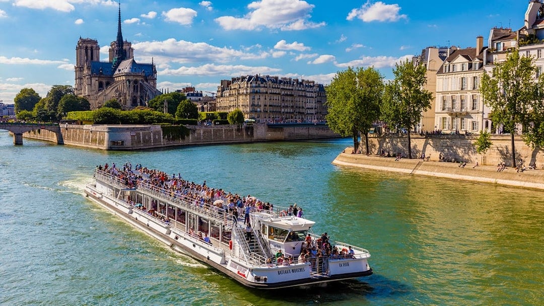 Seine River cruise boat with tourists near Notre-Dame Cathedral, Paris.