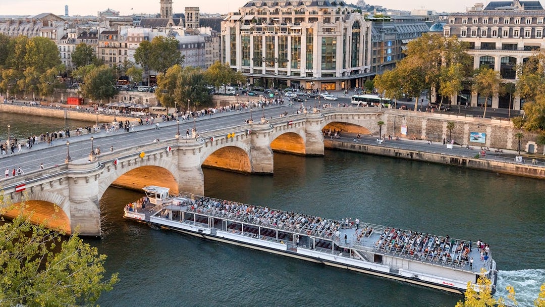 Seine River cruise boat passing under Pont Neuf in Paris with passengers enjoying the view.