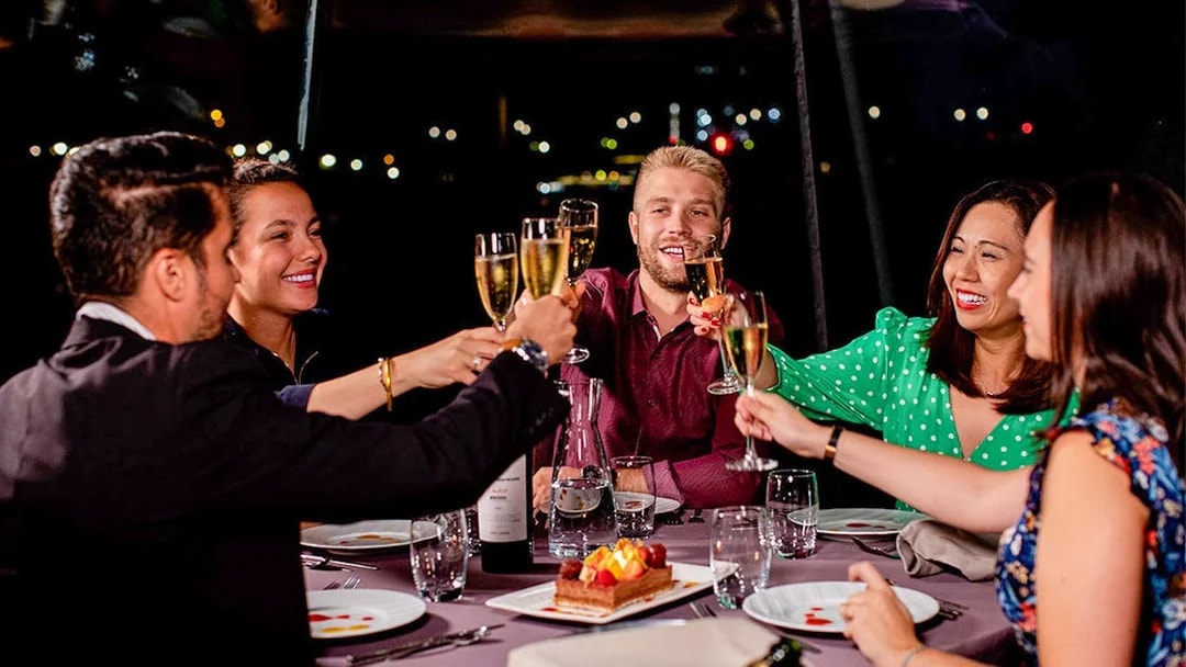 Guests toasting with champagne on a Seine River dinner cruise at night.