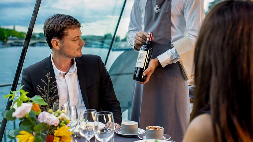 Server presenting wine to guests on a Seine River dinner cruise.