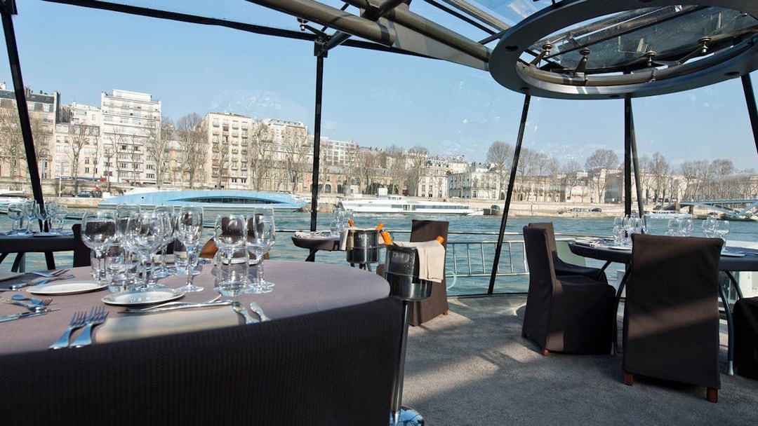 Seine River cruise dining setup with wine glasses and Parisian buildings in view.