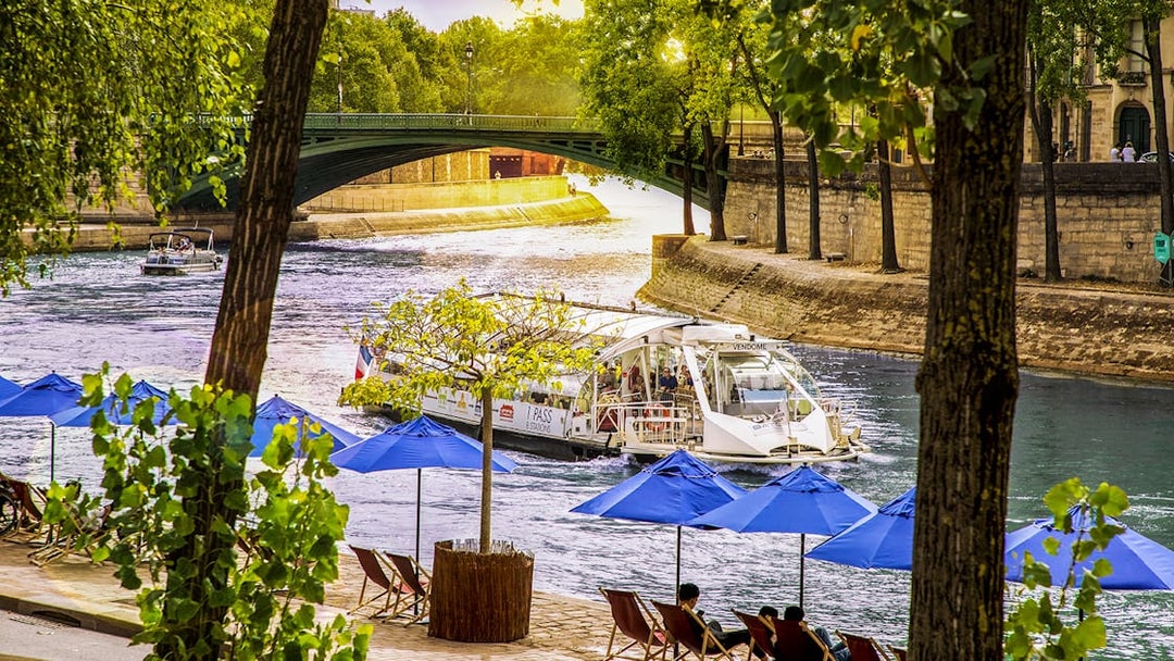 Batobus cruising on the Seine River in Paris with blue umbrellas and a bridge in view.
