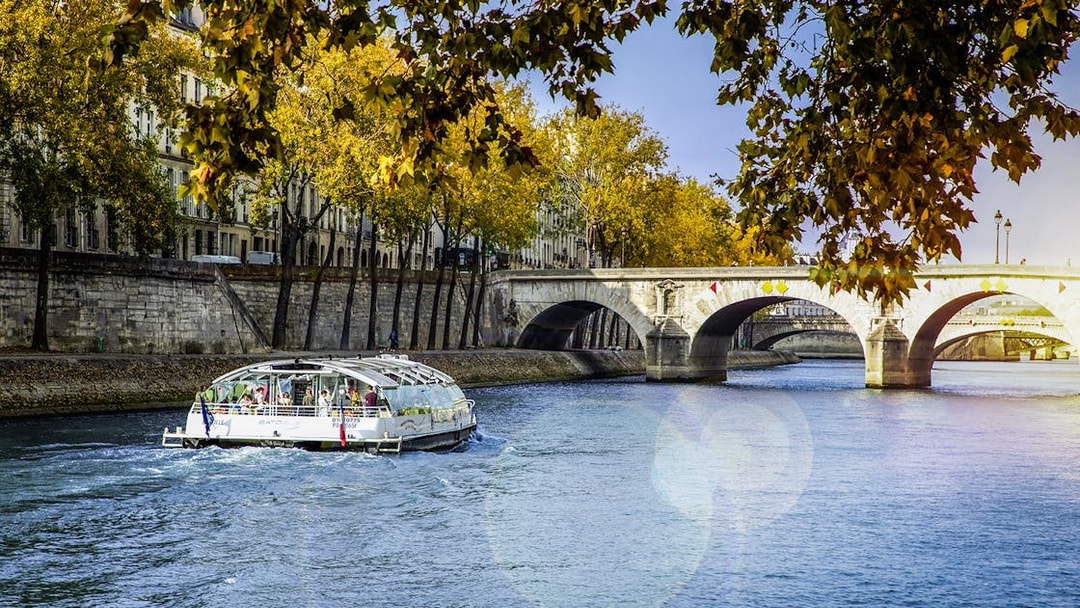 Seine River cruise boat near Paris bridge with autumn trees.