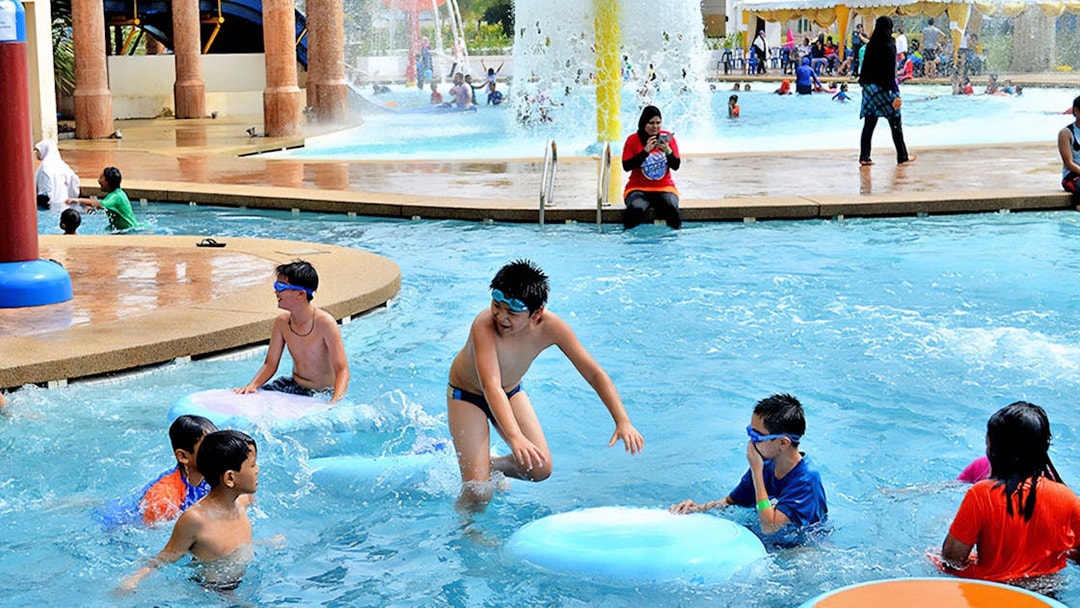 Children playing in the pool at Bayou Lagoon Water Park with slides and fountains in the background.