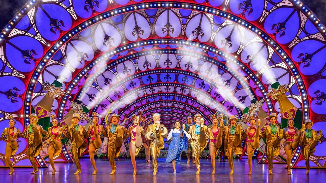 Performers in a "Beauty and the Beast" stage show with vibrant costumes and illuminated arches.