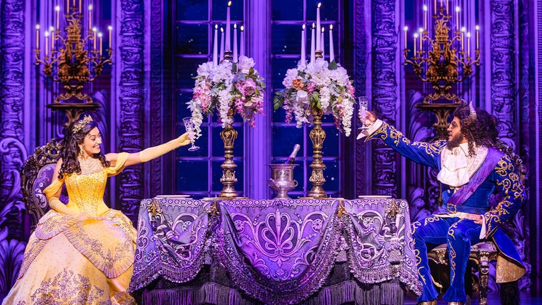 Belle and Beast toasting at an elegant table during a Beauty and the Beast performance.