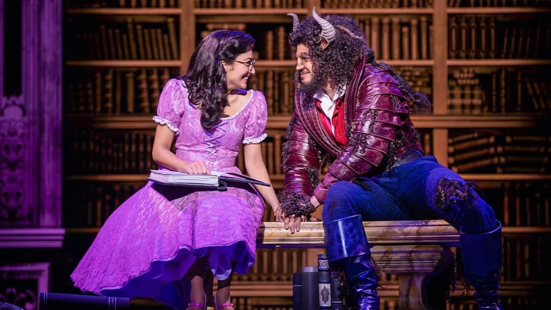 Belle and Beast sharing a moment in a library setting during a Beauty and the Beast performance.
