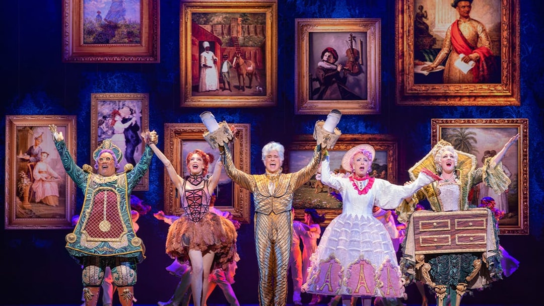 Performers in colorful costumes on stage during a Beauty and the Beast musical scene.