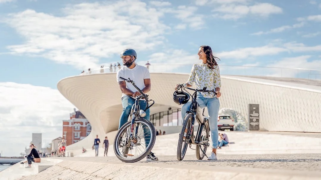 Tourists on ebikes by riverside near modern architecture in Lisbon.