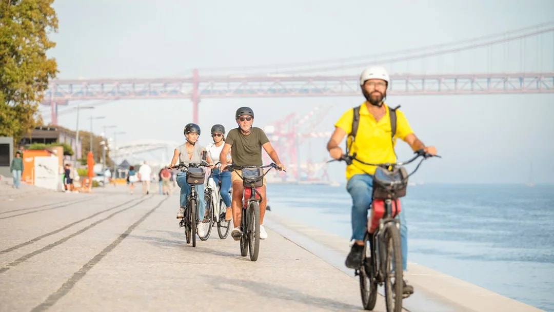 Cyclists ride along the waterfront under Lisbon's 25th of April Bridge.