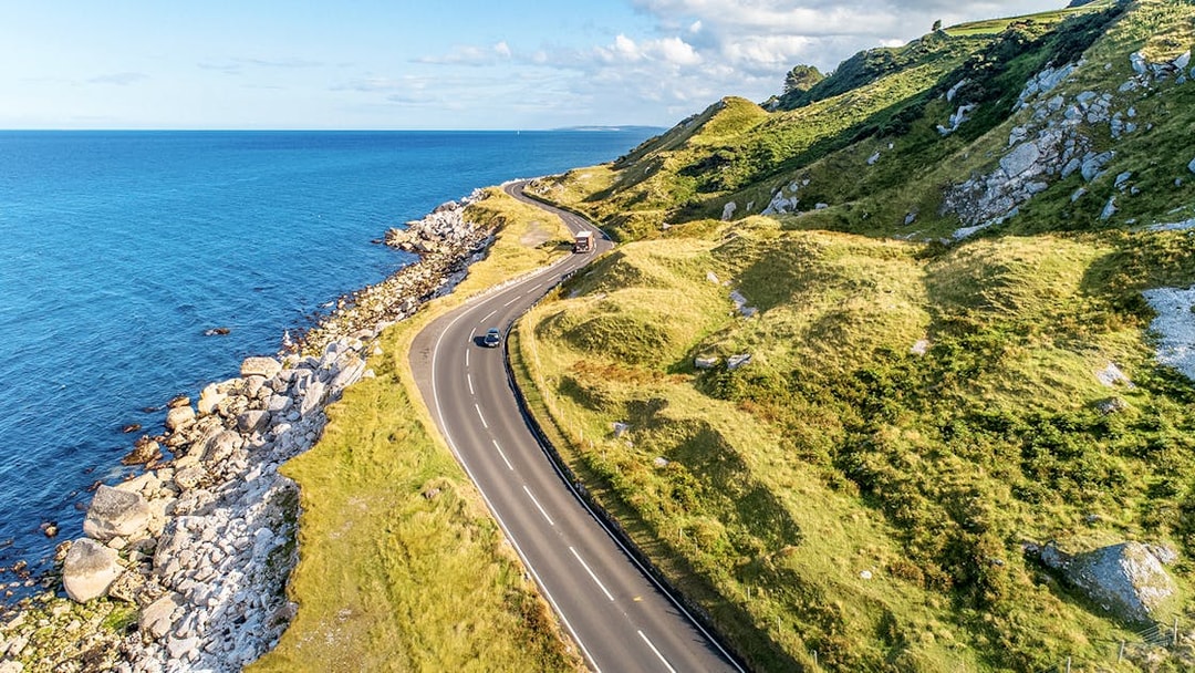 Coastal road along green hills and rocky shore on Game of Thrones tour in Belfast.