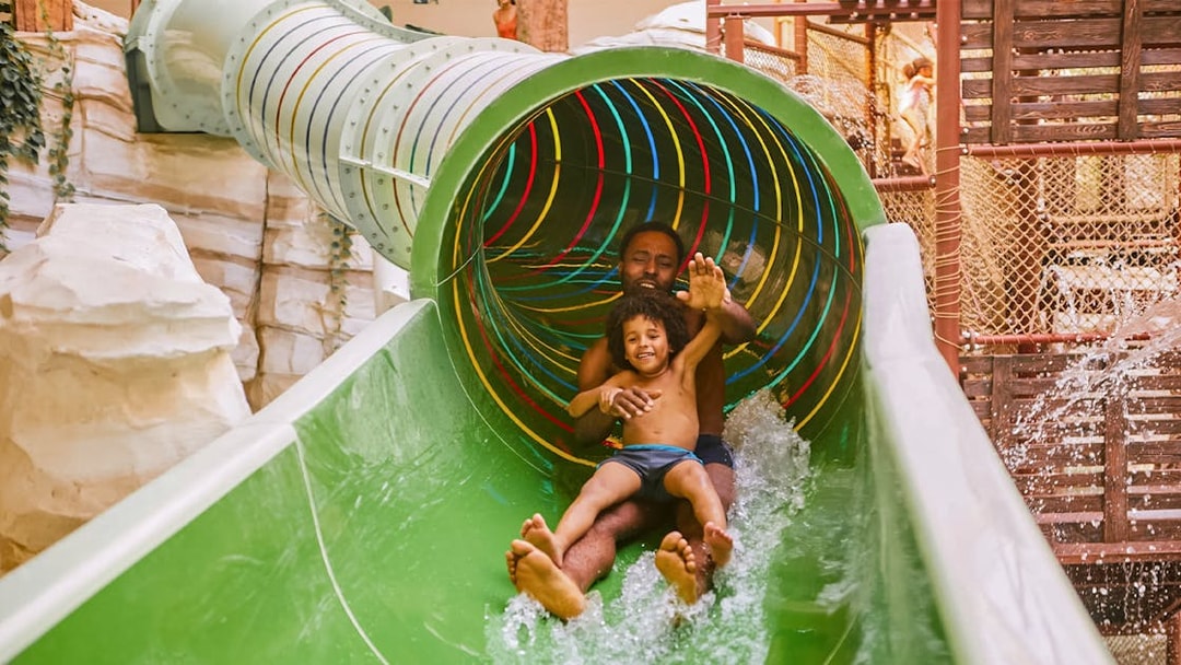 Father and child sliding down a colorful water slide at Bellewaerde Aquapark, Ypres.