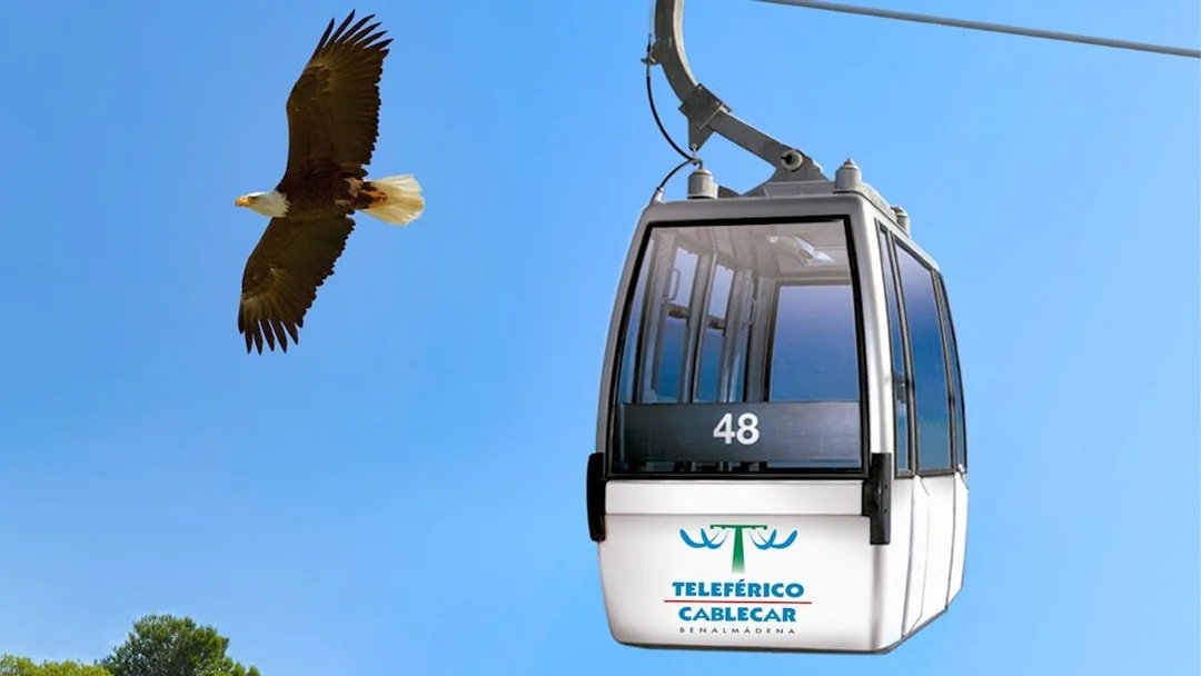 Benalmadena cable car with bird flying nearby against blue sky.