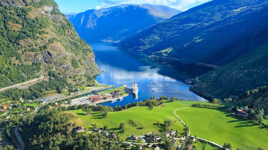 Nærøyfjord view with cruise ship docked, surrounded by mountains and green fields, part of Bergen day tour.