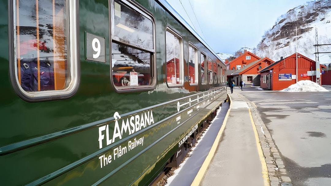 Flåm Railway train at snowy station with red buildings in Norway.