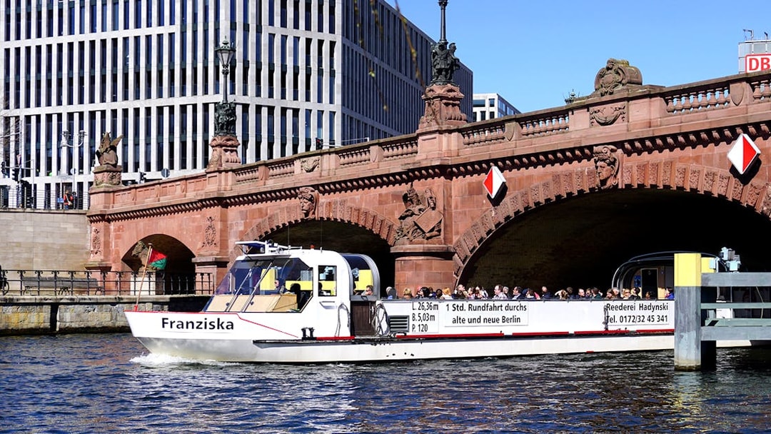 River cruise boat passing under a historic bridge in Berlin with tour guide.
