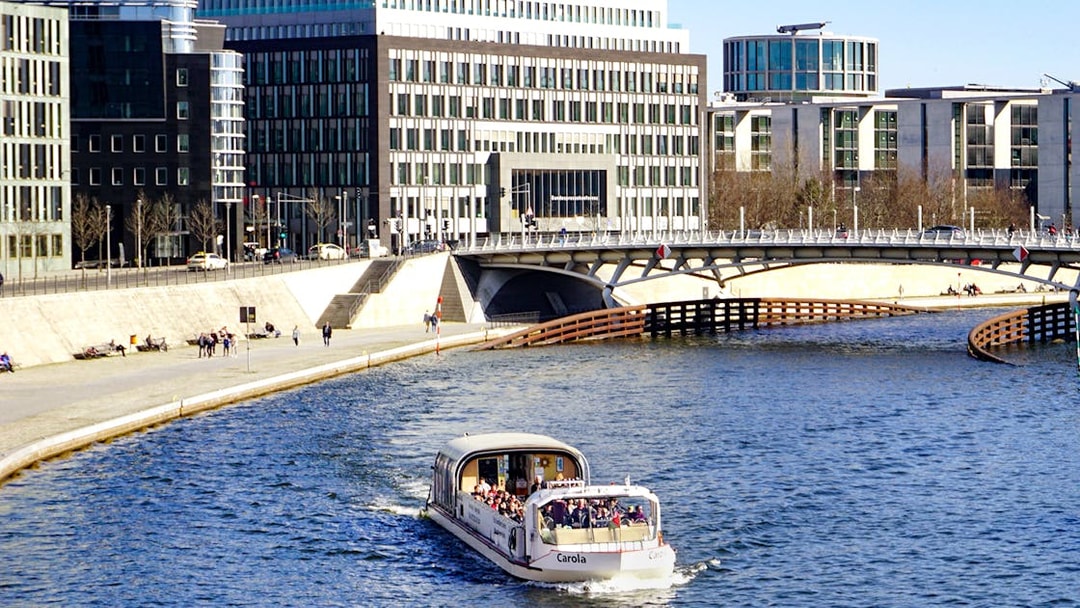 River cruise boat with tour guide on urban waterway near modern buildings.
