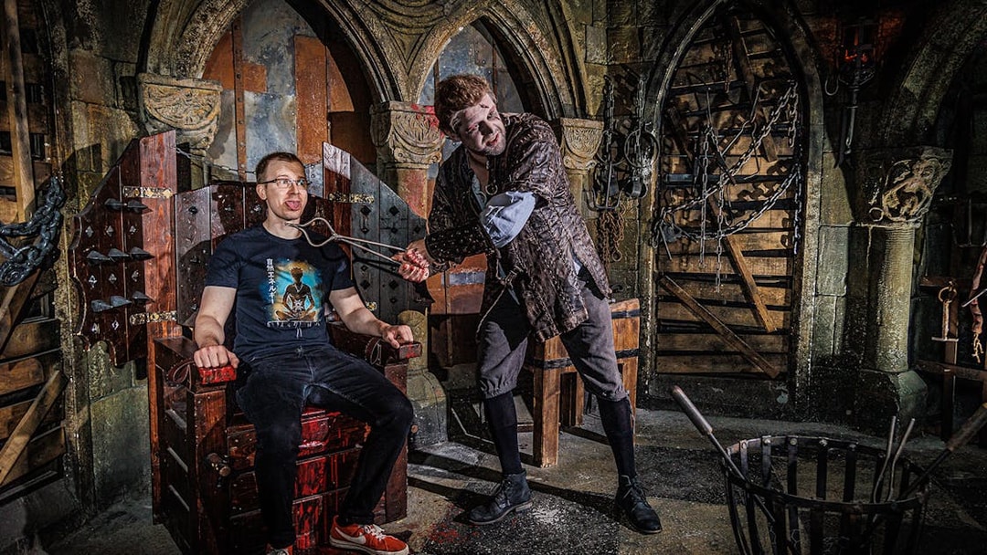 Torturer interacting with a visitor at the Berlin Dungeon in a medieval-themed setting.