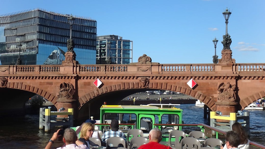 Sightseeing cruise boat passing under a historic bridge in East Berlin.