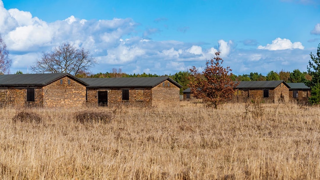 Soviet Camp No. 7 buildings in Sachsenhausen, surrounded by grass and trees under a blue sky.