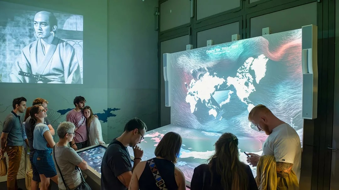 Visitors engaging with interactive display at Samurai Museum, featuring historical samurai imagery.