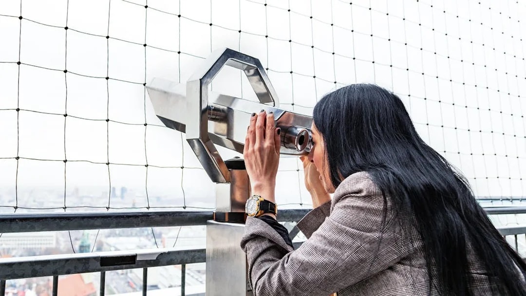 Woman using binoculars to view Berlin TV Tower from observation deck.