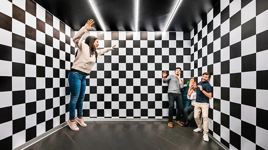 Visitors experiencing optical illusion in the Ames Room at Illuseum Berlin.